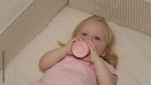 child in the bed eats from the bottle. photo