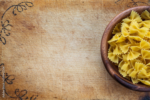 farfalle macaroni pasta in a wooden bowl on a cutting wooden board, texture background with a side. Close-up with the top. Free space for text.