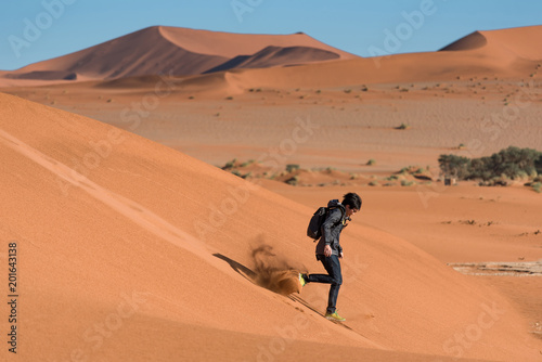Young Asian man dress in black and carrying backpack running down on sand dune in Namib desert of Namibia  Africa