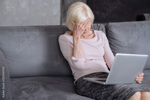 Elderly busy woman working on laptop and having headache. photo