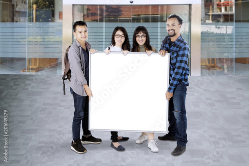 Group of college students holding a white board with copy space © Creativa Images