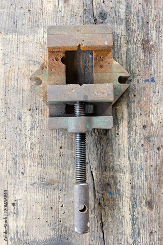 Old, dirty screw press against wooden plank. Tool series.