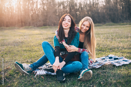 Two young female sitting on the grass at sunset. Best friends