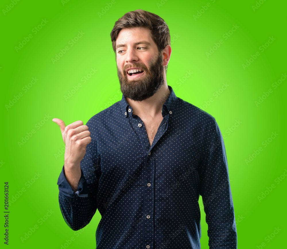 Young hipster man with big beard pointing away side with his finger over green background Young hipster man with big beard pointing away side with his finger over green background