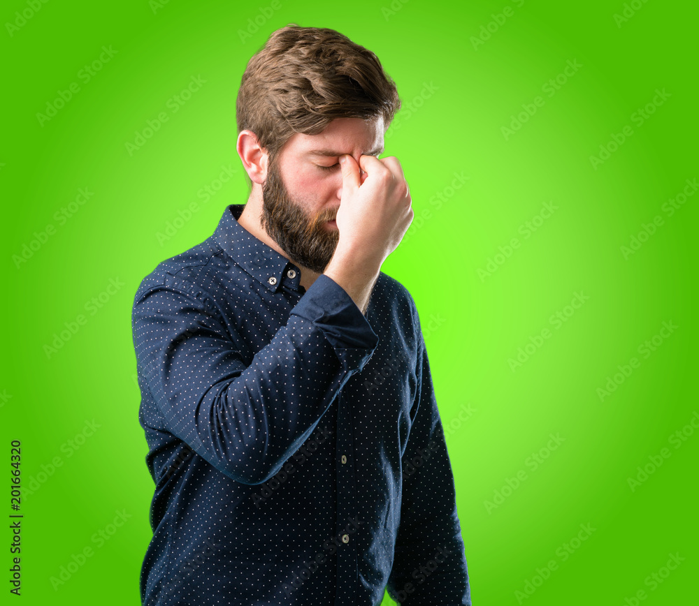 Young hipster man with big beard with sleepy expression, being overworked and tired, rubbes nose because of weariness over green background Young hipster man with big beard with sleepy expression, being overworked and tired, rubbes nose because of weariness over green background