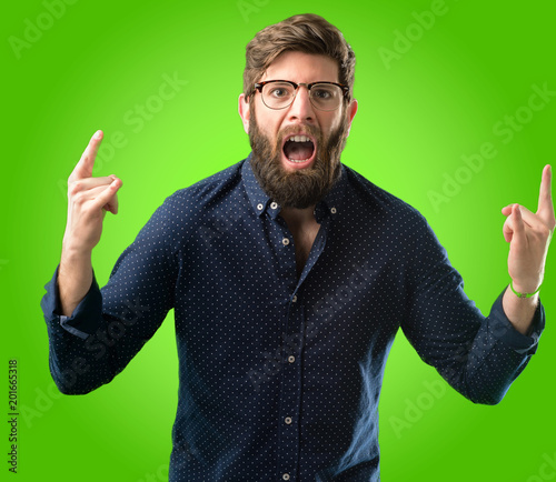 Young hipster man with big beard making rock symbol with hands, shouting and celebrating over green background