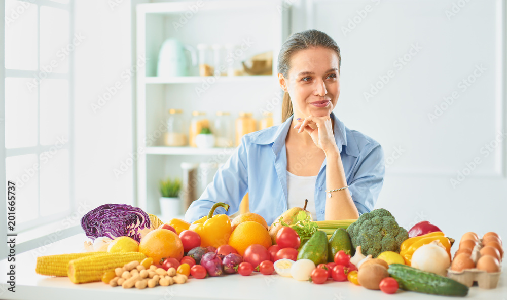 happy young housewife sitting in the kitchen preparing food from a pile of diverse fresh organic fruits and vegetables happy young housewife sitting in the kitchen preparing food from a pile of diverse fresh organic fruits and vegetables