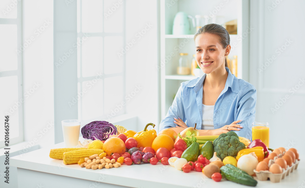 happy young housewife sitting in the kitchen preparing food from a pile of diverse fresh organic fruits and vegetables happy young housewife sitting in the kitchen preparing food from a pile of diverse fresh organic fruits and vegetables