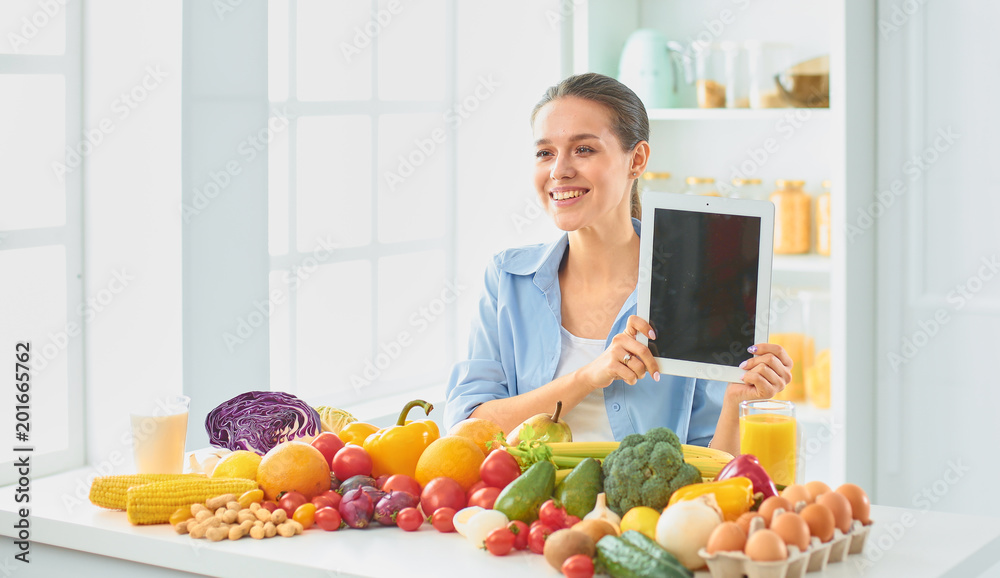 happy young housewife sitting in the kitchen preparing food from a pile of diverse fresh organic fruits and vegetables happy young housewife sitting in the kitchen preparing food from a pile of diverse fresh organic fruits and vegetables