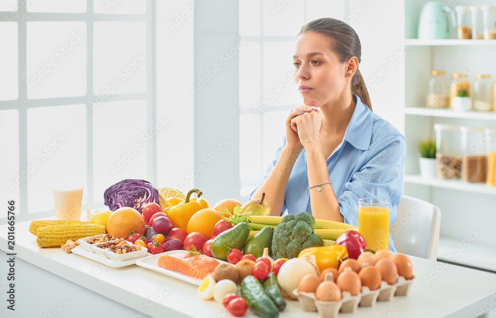 happy young housewife sitting in the kitchen preparing food from a pile of diverse fresh organic fruits and vegetables happy young housewife sitting in the kitchen preparing food from a pile of diverse fresh organic fruits and vegetables