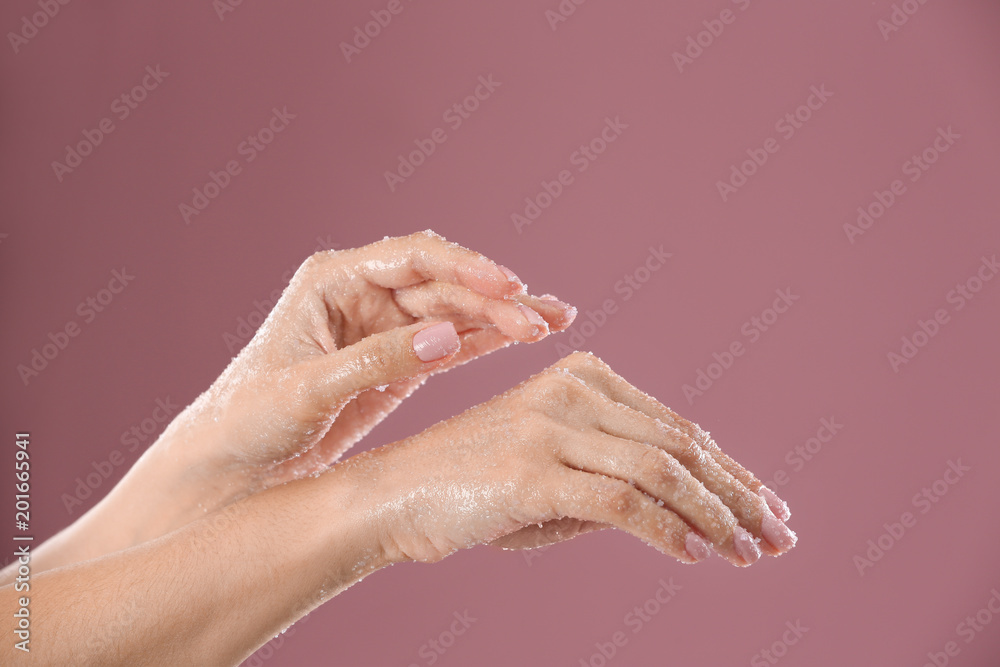Fototapeta premium Young woman applying natural scrub on hands against color background