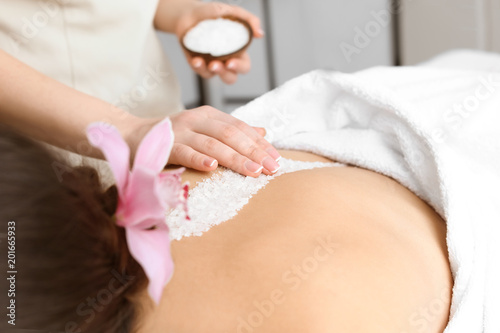 Young woman having body scrubbing procedure with sea salt in spa salon  closeup