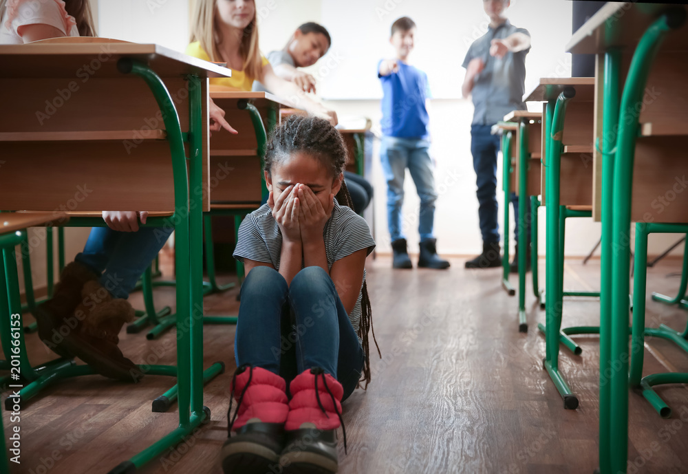 Bullied African American girl sitting on floor in classroom Bullied African American girl sitting on floor in classroom
