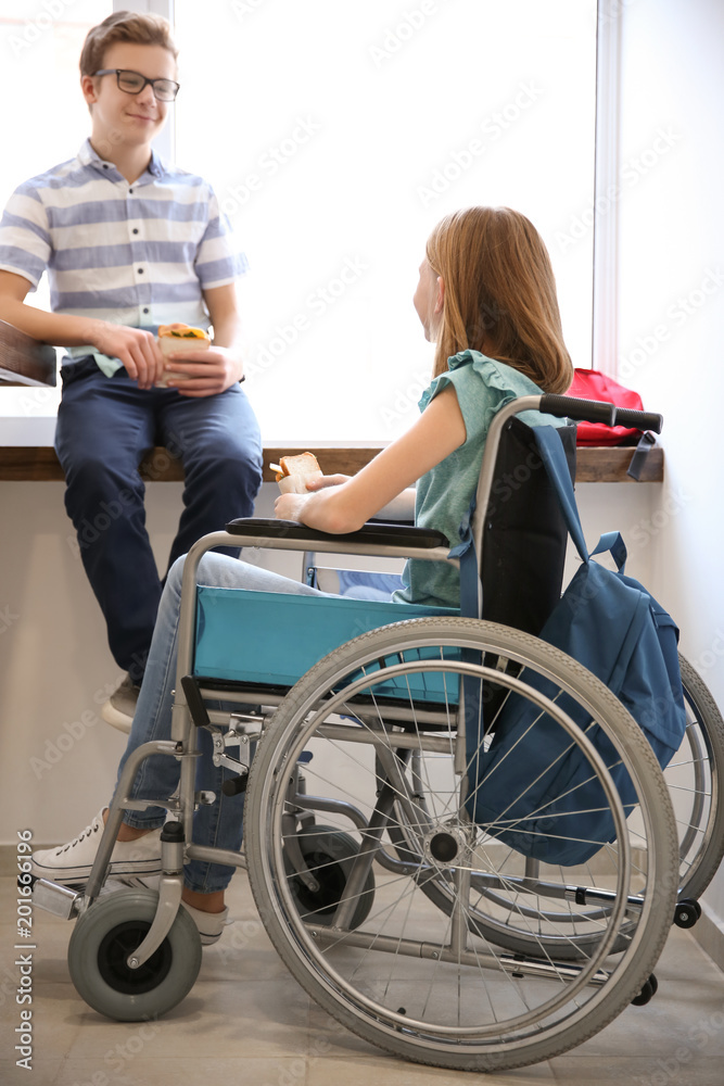 Teenage girl in wheelchair with boy eating sandwiches at school corridor Teenage girl in wheelchair with boy eating sandwiches at school corridor