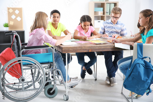 Teenage girl in wheelchair with classmates studying at school photo