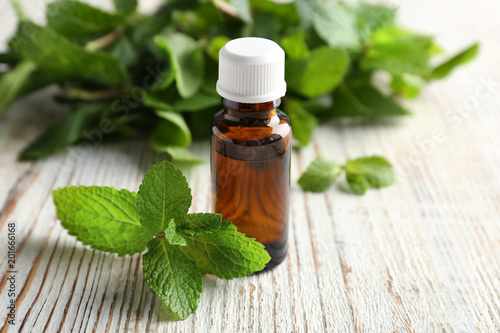 Bottle of essential oil with mint leaves on wooden table