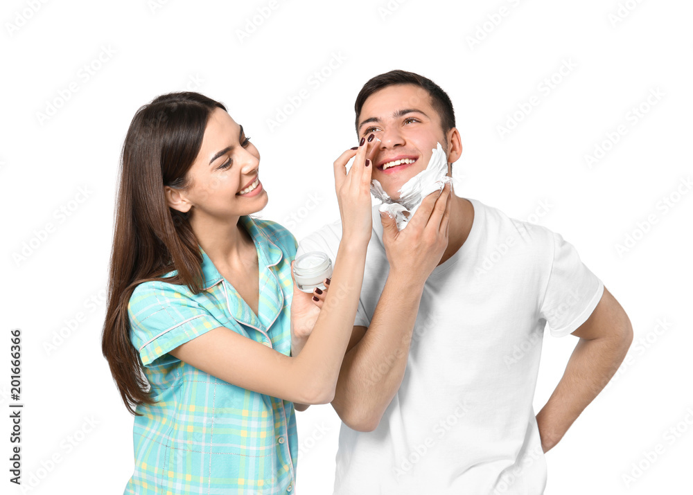 Young man shaving and his girlfriend applying face cream on light background Young man shaving and his girlfriend applying face cream on light background