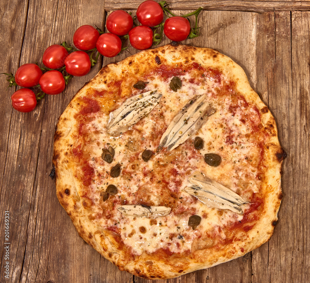 Homemade fresh delicious gourmet pizza Romana whit anchovies,capers and oregano,Tasty italian pizza isolated on wooden table, close up