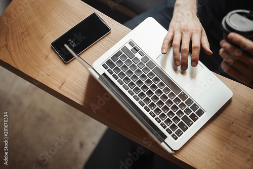 Young man is working on laptop and drinking coffee from black cup