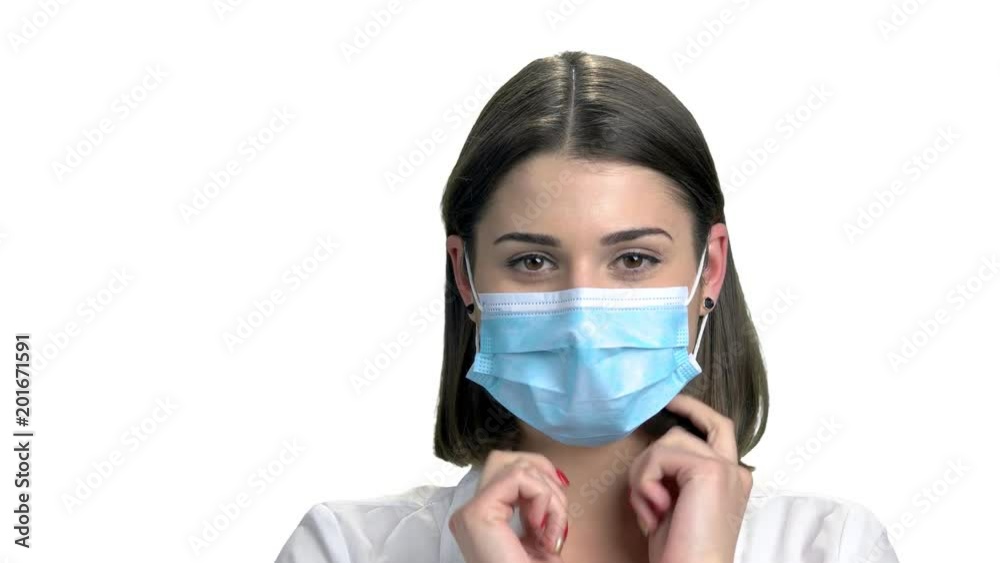 Close up young nurse putting on mask. Portrait of pretty smiling doctor puts on face mask on white background. People, medicine, healthcare. Close up young nurse putting on mask. Portrait of pretty smiling doctor puts on face mask on white background. People, medicine, healthcare.