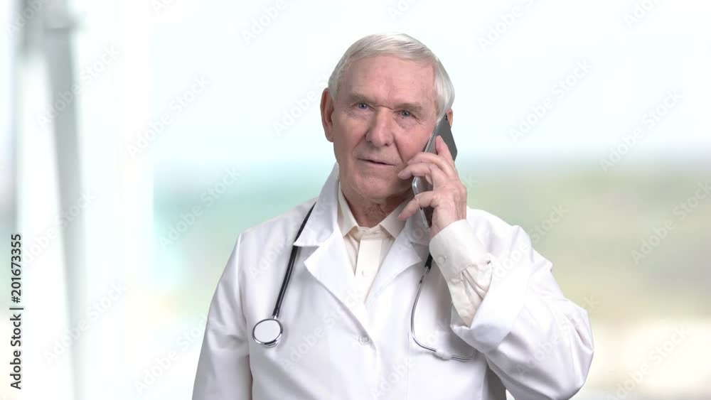 Old smiling doctor talking on phone. Senior therapist having converstation on phone, bright abstract blurred background. Old smiling doctor talking on phone. Senior therapist having converstation on phone, bright abstract blurred background.