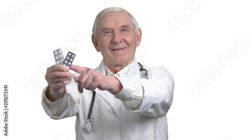 Senior old grey hair doctor in uniform pointing a medicine in strip. Portrait of elder man with white coat and stethoscope in white isolated background. photo