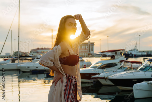 luxurious long-haired girl in stylish summer clothes posing in the seaport in the rays of the evening sun