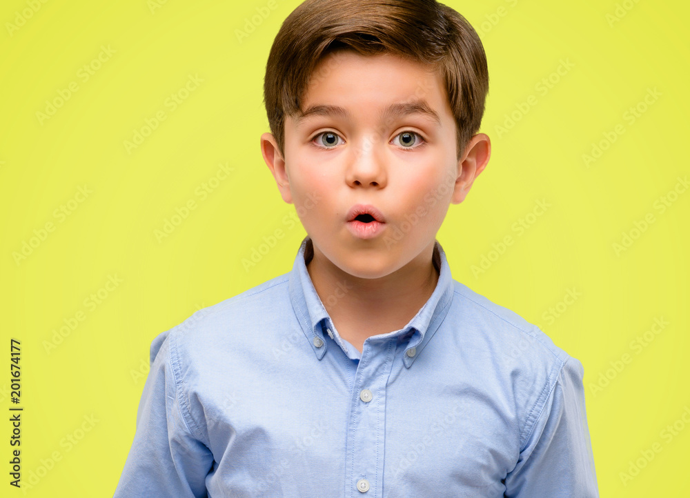 Handsome toddler child with green eyes happy and surprised cheering expressing wow gesture over yellow background Handsome toddler child with green eyes happy and surprised cheering expressing wow gesture over yellow background
