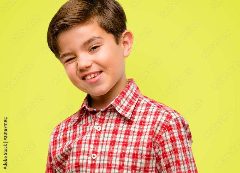 Handsome toddler child with green eyes blinking eyes with happy gesture over yellow background Handsome toddler child with green eyes blinking eyes with happy gesture over yellow background