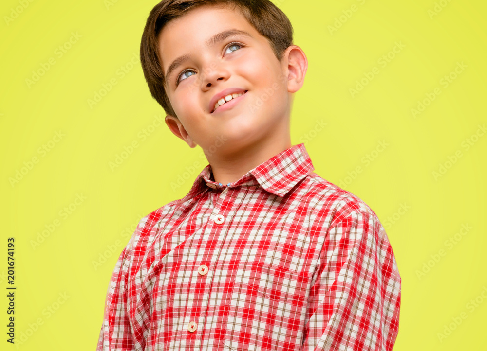 Handsome toddler child with green eyes confident and happy with a big natural smile laughing looking up over yellow background Handsome toddler child with green eyes confident and happy with a big natural smile laughing looking up over yellow background