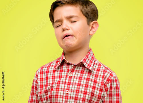 Handsome toddler child with green eyes crying depressed full of sadness expressing sad emotion over yellow background