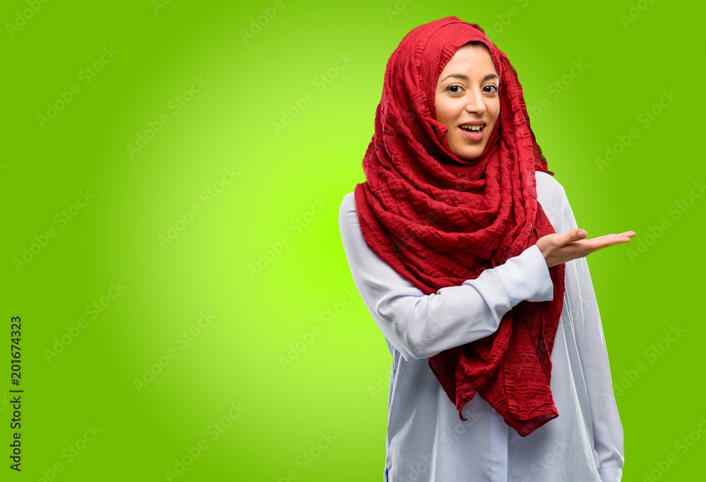 Young arab woman wearing hijab holding something in his empty hand Young arab woman wearing hijab holding something in his empty hand