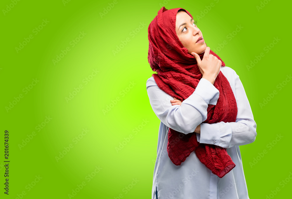 Young arab woman wearing hijab thinking and looking up expressing doubt and wonder