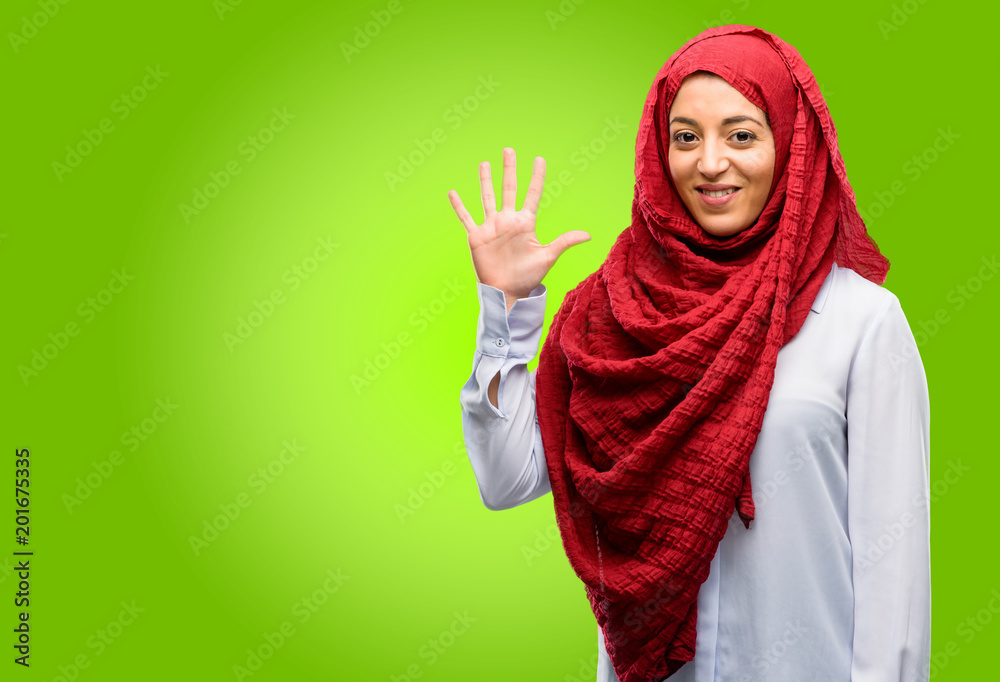 Young arab woman wearing hijab raising his finger, is the number five Young arab woman wearing hijab raising his finger, is the number five