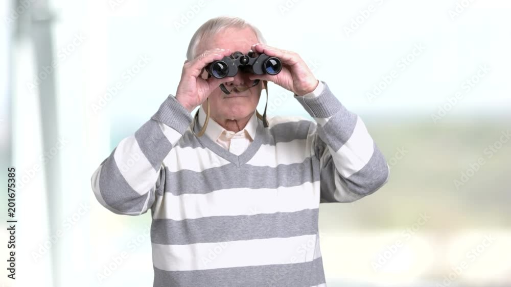 Senior man looking through a pair of binoculars. Grandfather looking into binoculars and looking for something, blurred background. Senior man looking through a pair of binoculars. Grandfather looking into binoculars and looking for something, blurred background.