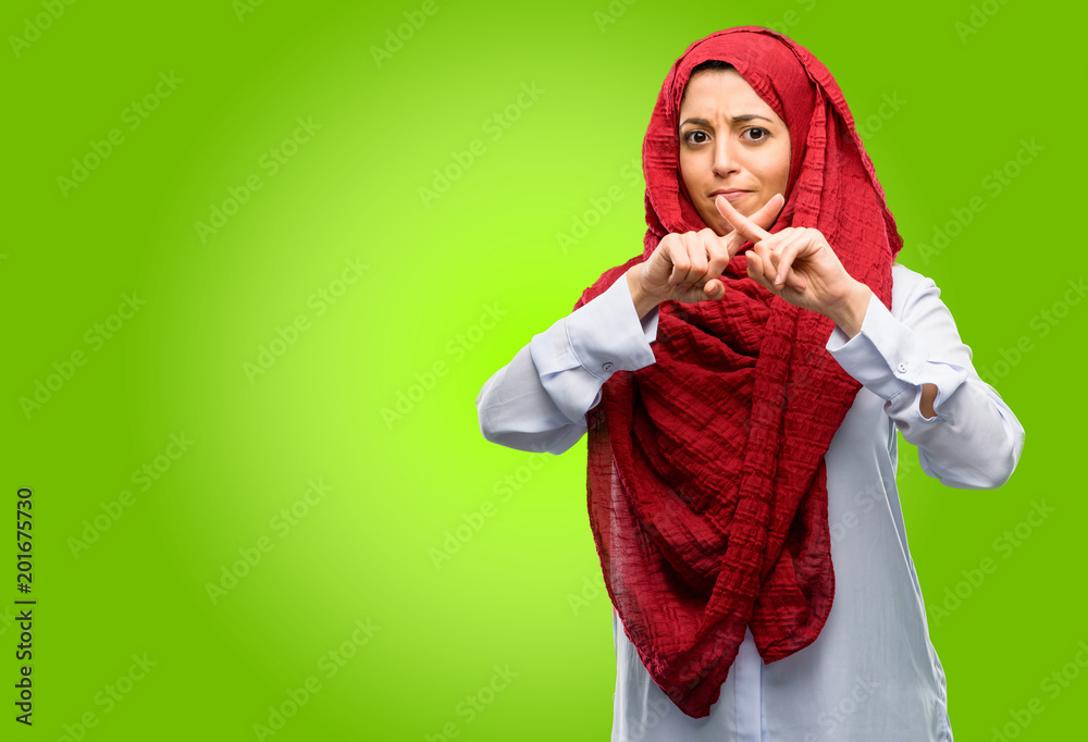 Young arab woman wearing hijab annoyed with bad attitude making stop sign with hand, saying no, expressing security, defense or restriction, maybe pushing