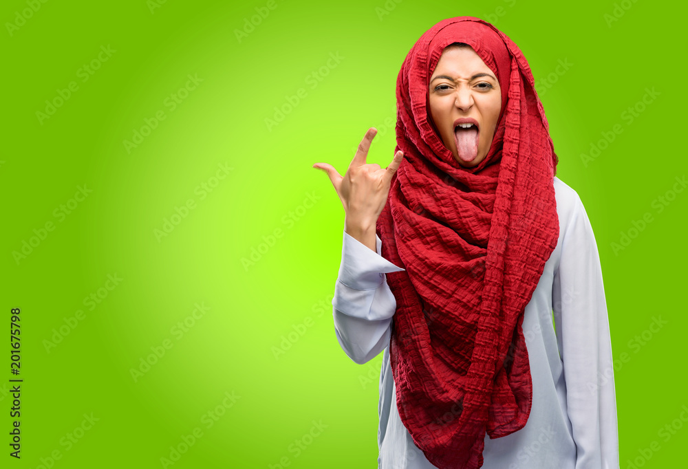 Young arab woman wearing hijab making rock symbol with hands, shouting and celebrating with tongue out Young arab woman wearing hijab making rock symbol with hands, shouting and celebrating with tongue out