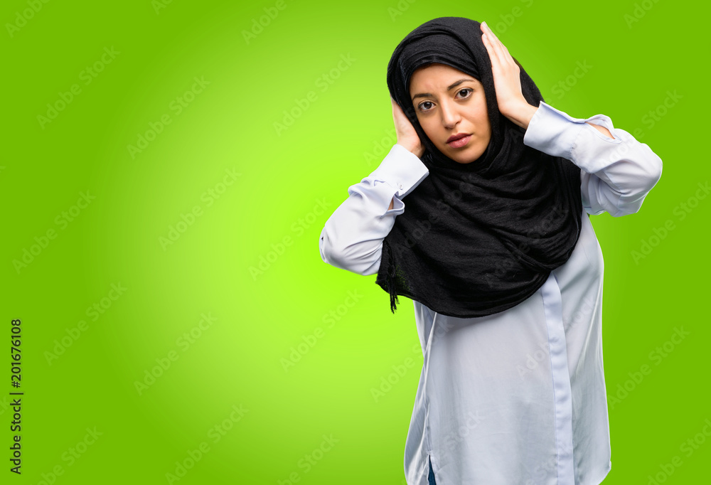 Young arab woman wearing hijab covering ears ignoring annoying loud noise, plugs ears to avoid hearing sound. Noisy music is a problem. Young arab woman wearing hijab covering ears ignoring annoying loud noise, plugs ears to avoid hearing sound. Noisy music is a problem.