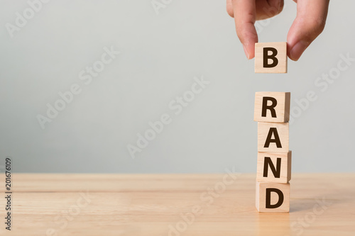 Hand of male putting wood cube block with word “BRAND” on wooden table. Brand building for success concept photo