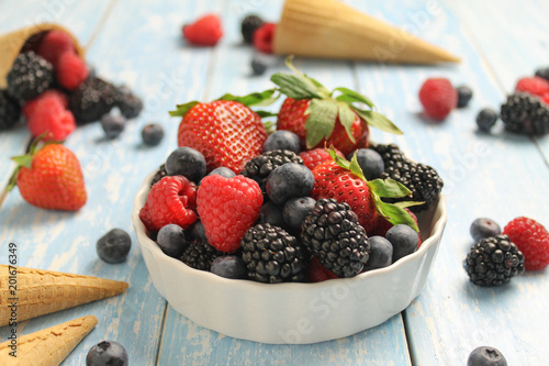 Mix fresh berries in a white bowl on a wooden background. Various berries in a sugar cones.