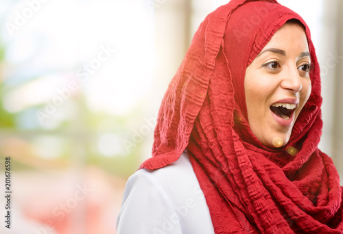 Young arab woman wearing hijab happy and surprised cheering expressing wow gesture