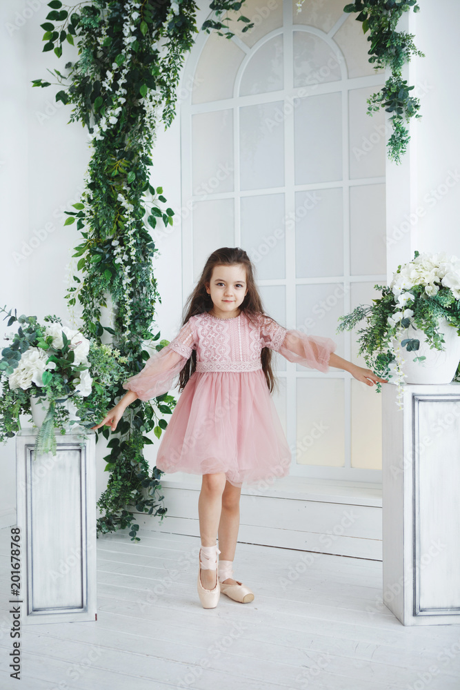 A young ballerina in a pink dress is standing in pointe shoes framed by green branches