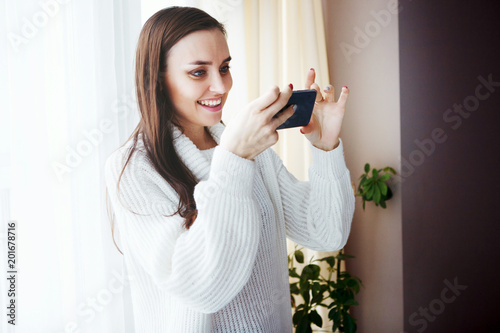 Young cute girl with long hair in a white sweater makes a photo on a smartphone