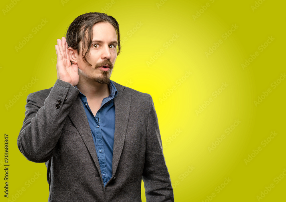 Handsome young man holding hand near ear trying to listen to interesting news expressing communication concept and gossip Handsome young man holding hand near ear trying to listen to interesting news expressing communication concept and gossip