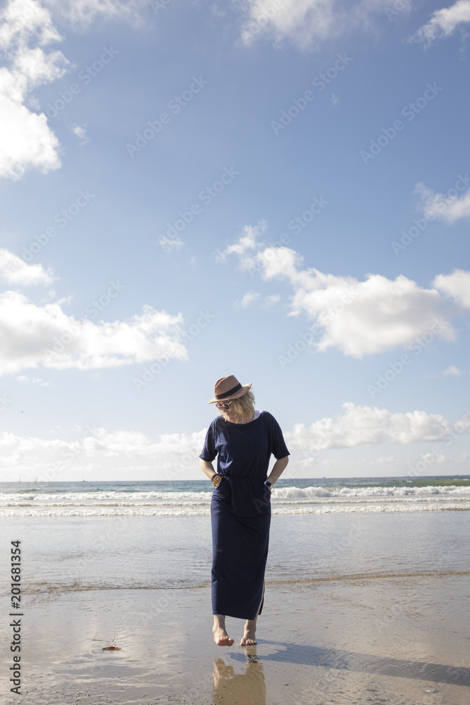Woman wearing black dress and hat walking casually along beach Woman wearing black dress and hat walking casually along beach