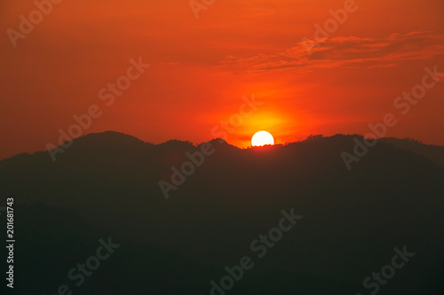 Red and orange warm sunlight in the sky during sunset with mountain  range in foreground  shade and shadow  sunset sunrise