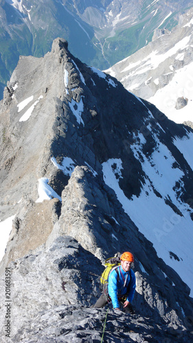 male mountain climber on his way to a high alpine summit on a steep and exposed rock ridge on a beautiful summer day photo
