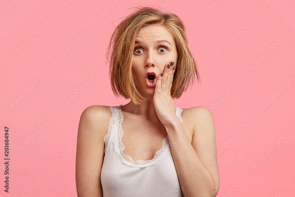 Entangled pretty female model looks with shocking expression at camera, keeps hand on cheek, wears nightdress, woke up very late, isolated over pink background. Facial expressions and reaction Entangled pretty female model looks with shocking expression at camera, keeps hand on cheek, wears nightdress, woke up very late, isolated over pink background. Facial expressions and reaction