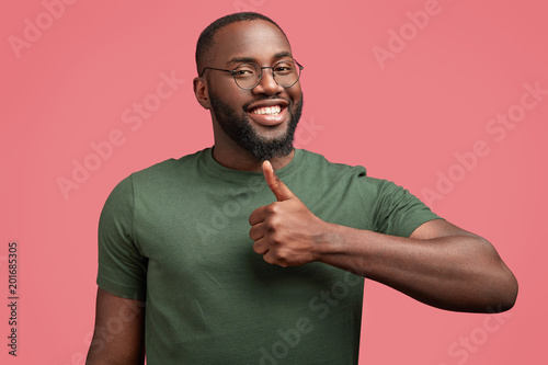 People and body language concept. Happy satisfied African American guy shows approval sign or ok gesture, likes something, dressed in casual green t shirt. That`s fine, I completely agree with you