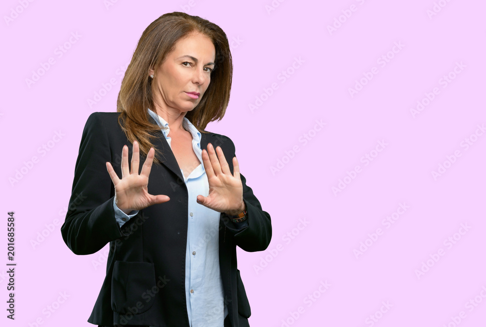 Middle age business woman annoyed with bad attitude making stop sign with hand, saying no, expressing security, defense or restriction, maybe pushing Middle age business woman annoyed with bad attitude making stop sign with hand, saying no, expressing security, defense or restriction, maybe pushing